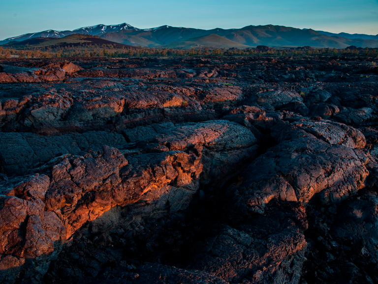 A close-up shot of a folded, waving sea of lava rock, with mountains in the far distance.